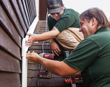 Two individuals installing a heat pump on a roof